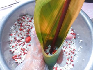 9、红豆红枣牛角粽,在牛角漏斗中舀入1/3的红豆、糯米，拿筷子捅实；