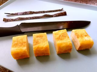 20、日式厚蛋烧,等蛋卷凉了以后再用刀切成块，这样不容易切坏。剪几条海苔条，用来包裹切好的厚蛋烧