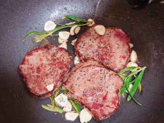 13、迷迭香黑胡椒牛排,再撒上一些黑胡椒碎、放入一些蒜片。这面煎至60秒继续翻面。