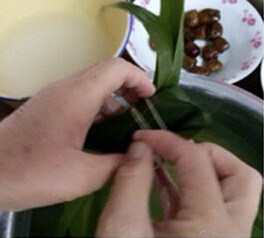 4、蜜枣花生粽,把粽叶尾部对折后折到一边，用粽绳将粽子拦腰捆好