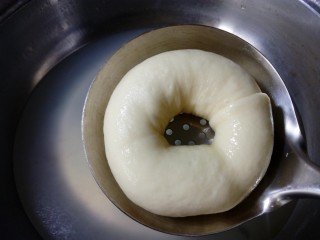 22、原味贝果（超详细版）,将面团用漏勺捞出，沥去水分。也可以把捞出的面团放在布上，吸干底部水分，水份太多会粘烤盘也影响口感。  这时煮过的面团表皮会微皱，后面烤的时候面团会发胀把表面撑起来的。