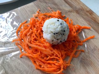 15、日式手鞠壽司飯團,胡蘿蔔鋪在保鮮膜上，手沾一點點水捏一個大小合適的小飯團放在胡蘿卜上面。