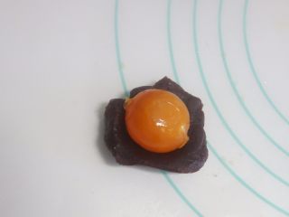 6、豆沙广式月饼制作方法,将称好的馅料搓圆压扁，放上咸蛋黄，用馅料把咸蛋黄包起，记住用虎口慢慢推，包裹均匀。最后揉圆。