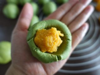 8、蛋黄肉松青团（麦青粉版）,小面团按一个坑，装入馅儿，用虎口慢慢捏拢，包起来搓圆。（做法同包汤圆）