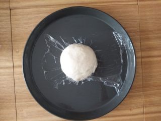 3、薄脆辣牛披萨,面团取出放披萨盘上盖上保鲜膜醒15分钟