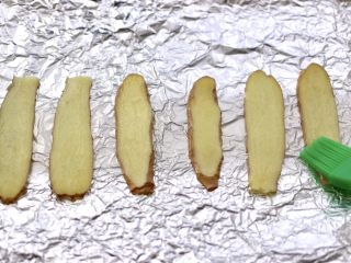 10、香辣孜然烤鱼,烤盘上铺上锡纸,放入姜片,这是为了在烤鱼的时候,不让鱼皮脱落掉,软化后的黄油,用刷子蘸少许把姜片刷一层薄薄的黄油。