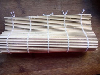 11、樱花寿司,拖动保鲜膜把海苔至于竹帘边缘,然后对折成水滴状,两手用力压紧。