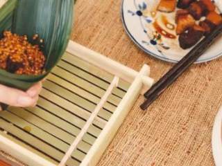 4、【粽子周·普洱肉粽】,粽叶窝成漏斗状，填米放入炖好的普洱肉，再填些米，包紧系上