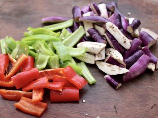 3、干煸烤肠茄条双椒,把茄子洗净后切成条，青红尖椒去籽后切成条。