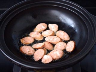 5、干煸烤肠茄条双椒,砂锅中倒入花生油烧热，把烤肠放入锅中开始小火慢慢煎制。