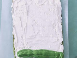 18、【网上厨房独家】丸久小山园名物蛋糕卷—复刻,蛋糕片撕掉烤纸的一面向上，淡奶油均匀抹在蛋糕片上，靠近自己的这边稍多一些，另一边少一点，抹茶奶油重叠的挤3条在靠近自己的这边，用抹刀整理好，借助擀面杖卷成卷