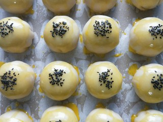 25、蛋黄酥,然后依次刷上蛋黄水，放进烤箱150°烤五分钟定型，再取出再刷上一次蛋黄水，撒上少许芝麻