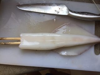8、韩式辣烤鱿鱼,在砧板上平铺鱿鱼筒，在鱿鱼筒内插入一双筷子。垫上筷子，用刀切下去的时候，碰到筷子就停下来。这样下面的鱿鱼面不会被切断。