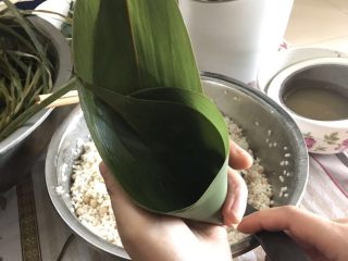 6、肉粽子,两片叶子卷成图中形状，加入一勺前面拌好的糯米，中间加入一块猪肉，再放入一勺前面拌好的糯米（具体以叶子大小决定）