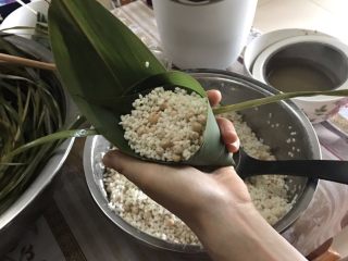 7、肉粽子,放完糯米后，用棕叶的叶尖夹在两片粽子叶的中间，冒出来的棕叶尖不要太长