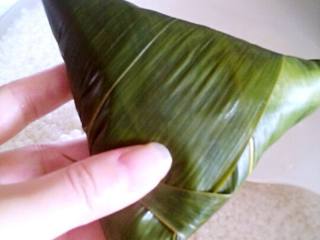 6、蜜枣粽子,然后再次加入米， 快满的的时候，灌入水，会自然流出后，粽子米会更紧实。按三角形卷起，如图。