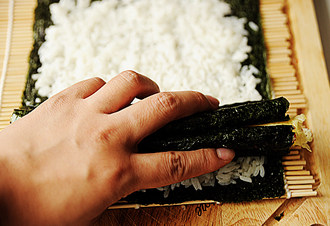 11、创意无限的花样寿司【小花寿司】,先在步骤10的白米饭的一端放两瓣花瓣寿司，然后在这两瓣花瓣的中上方放上花蕊，最后再将花蕊两旁放上两瓣花瓣，最顶部放上一瓣花瓣，用手扶住；