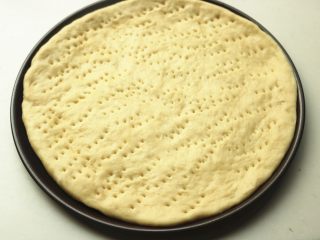 6、黑椒牛柳披萨,面胚放入披萨盘，整理一下边缘，用叉子叉出小孔，避免烤的时候鼓泡。