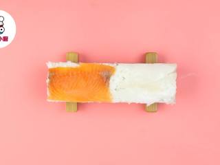 4、懒人免卷箱寿司,再在模具中铺一层寿司饭，放上海苔1片，再铺一层寿司饭，然后一半铺墨鱼片，一半铺三文鱼片，压实取出备用