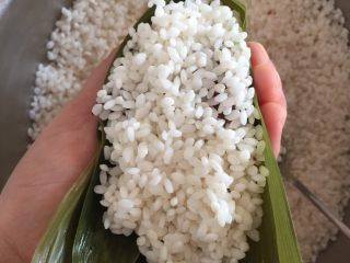 14、肉粽子,在添几勺米，把肉盖住，，整个过程用手托住粽叶，不要松开