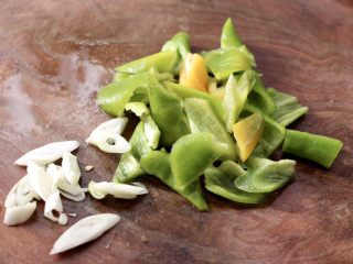 2、腊肠炒鸡蛋,把青尖椒用刀切成片，蒜苗切丝。