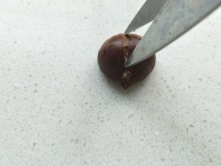 4、糖烤板栗,拿一个板栗，用剪刀竖着把板栗剪开口。