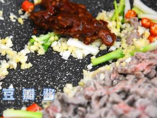 4、芹菜牛肉,变色的牛肉丝推至锅中的另一边，空出来的地方倒入葱白、小米椒、姜蒜末，一起炒香后再加入豆瓣酱和肉丝炒至上色。