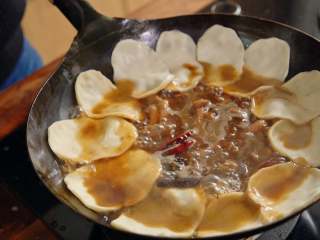 10、地锅鸡【曼食慢语】,将饼围着锅贴一圈,盖上锅盖,继续炖煮约15分钟。15分钟后开锅盖,加入炸过的蒜头,拌入鸡肉中,调整贴饼的位置,把它埋到汤里头