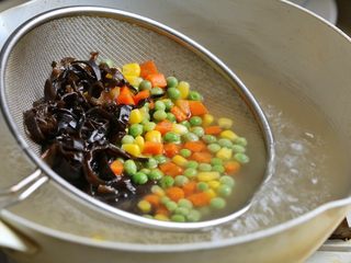6、缤纷虾仁蛋炒饭,水中加一勺盐和少许油,将胡萝卜丁,豌豆丁、玉米粒和黑木耳丝放入沸水中焯熟,捞出沥水备用。