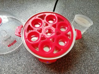 7、菠菜鸡蛋糕,准备好煮蛋器，放上蛋托盘，用量杯取最高水位的水加入到蒸盘里面。