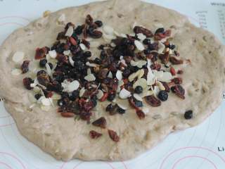 7、圣诞史多伦,取出发酵好的面团，稍微擀平，上面撒上一半的水果干和一半的杏仁片，用擀面杖将果干压实。