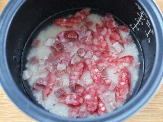 6、上海咸肉菜饭,将浸泡好的大米放入饭煲内胆中，添入比平时煮饭稍微少一点的清水，再放入腊肠和咸肉丁，放入饭煲内开始煮饭