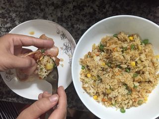 16、鸡翅包饭,一只手拿着去骨腌制好的鸡翅，另外一只手用勺子将炒好的饭塞进鸡翅里面，塞满就可以，不可以过涨，这样烤的时候，鸡翅会裂开的。