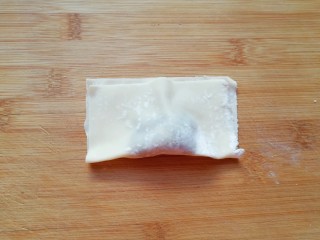 8、大馅馄饨,取一个馄饨皮放上肉馅,将馄饨皮对折,用两只手的大拇指和食指把有馅的地方捏挤一下,让馄饨馅团在一起。