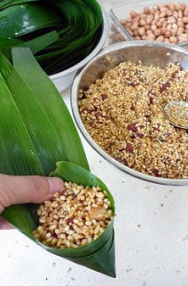 4、香浓里脊肉粽,将苇叶码齐后将宽头的一端窝成一个三角漏斗状，依次放入拌好的糯米、肉，中间放几粒花生米。