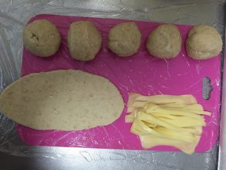 4、燕麦芝士贝果～,把小面团揉成椭圆形，再用擀面杖擀成椭圆形大面皮～将芝士切成条，容易包裹～