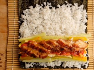 4、鳗鱼紫菜包饭,紫菜上平铺米饭，略微压实，放上配料，最好像图中这样两侧放黄瓜条，中间放鸡蛋，这样方便卷。