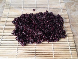 7、双糯米蒸饭包油条,在寿司帘上铺张保鲜膜、放上适量黑糯米饭