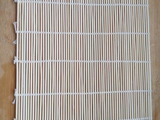 4、不拘一格吃寿司,将卷寿司的帘子平铺在案板上。