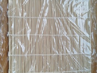 5、不拘一格吃寿司,铺上一层保鲜膜，记住，保鲜膜大小要比帘子大。