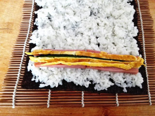 6、幸福的紫菜包饭,在靠近紫菜的一头摆好黄瓜，火腿和鸡蛋皮，
