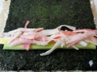 4、三文鱼寿司,将沾有米饭的海苔翻转放在竹帘上，当中放入黄瓜、鸡蛋皮、熟蟹肉，顺一边卷起卷紧。（海苔在里面）