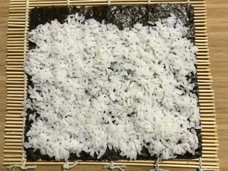 3、快手紫菜包饭,将温热的米饭平铺到上面，注意底部留出一部分不铺米饭。