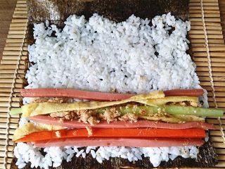 8、什锦火腿寿司,将饭团往四周推平，在下端摆放蛋皮、黄瓜、火腿、肉松和胡萝卜