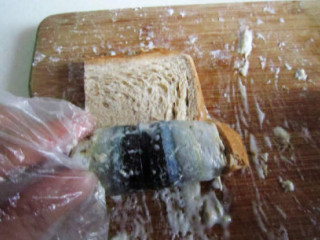 6、烤秋刀鱼吐司手卷,取一片吐司放与鱼肉上，鱼皮朝下放。然后从鱼尾部开始往头部卷制，在接头除，用牙签固定