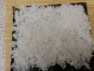 4、紫菜包饭,取竹帘，放上一片烤紫菜，再放上米饭，用沾水的大勺子，或者直接用沾水的手将米饭均匀地压实在紫菜上，只在不靠近自己的那一头留1cm的边沾合用(准备工作时，用来沾手或勺子用，这样米饭就不会沾手啦！)