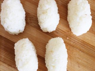 2、三文鱼握寿司,米饭趁热放入适量寿司醋拌匀，手蘸凉开水，取适量寿司饭捏成椭圆形饭团。