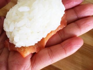 3、三文鱼握寿司,鱼片内面抹上一层薄薄的芥末，将鱼片抹有芥末的内面朝上，放上饭团。用手轻轻按压一下。