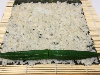 16、酱香味秋葵寿司(纯素版),放两根秋葵在米饭一端,用竹席卷上一点