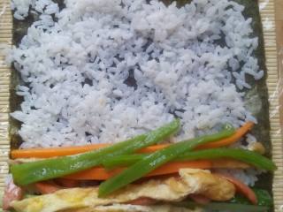 4、紫菜包饭,竹帘上放上保鲜膜，放上紫菜， 平铺一成米饭， 在摆好菜。